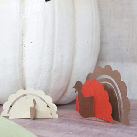 Paper cut out turkeys next to a white pumpkin