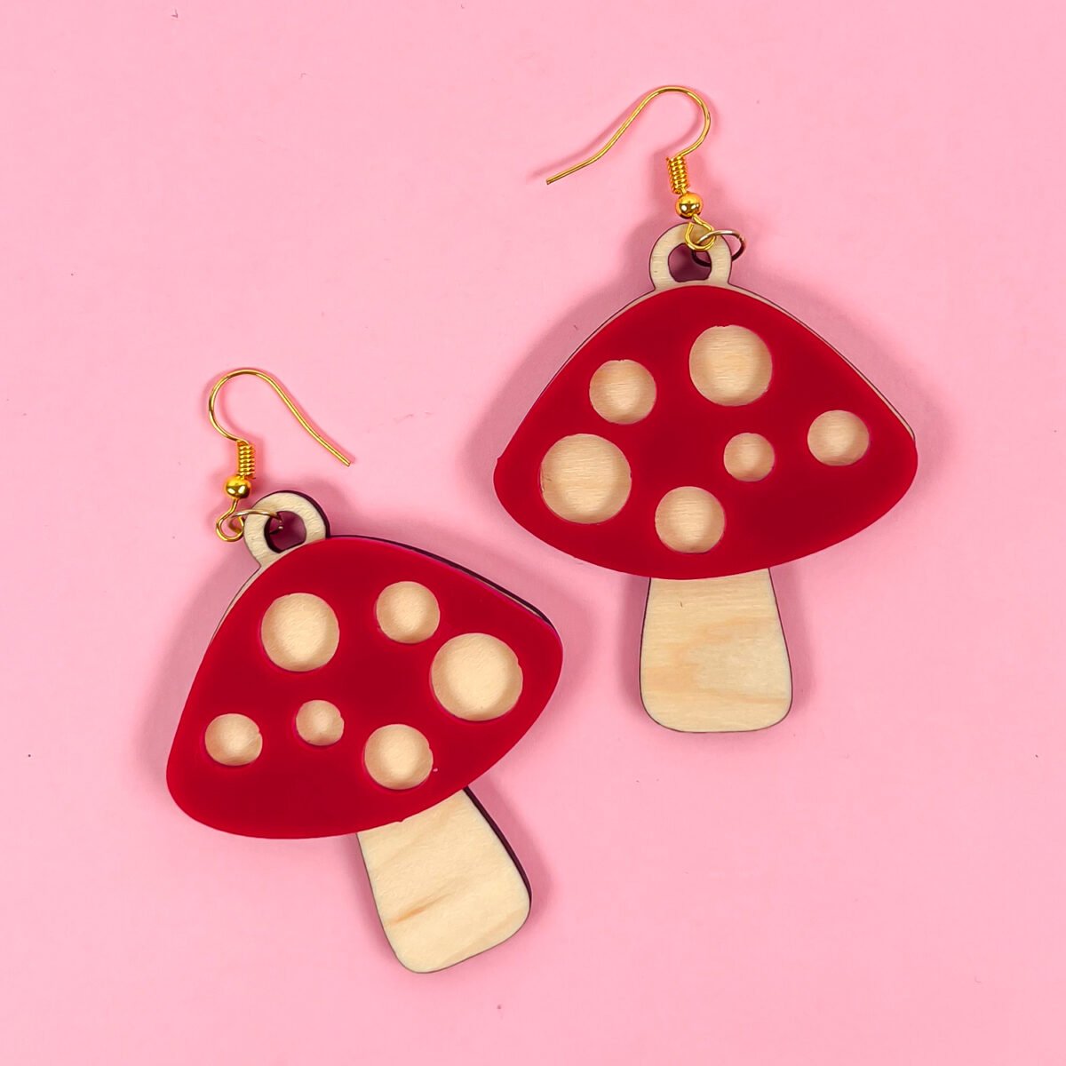 Red and wood mushroom earrings on pink background