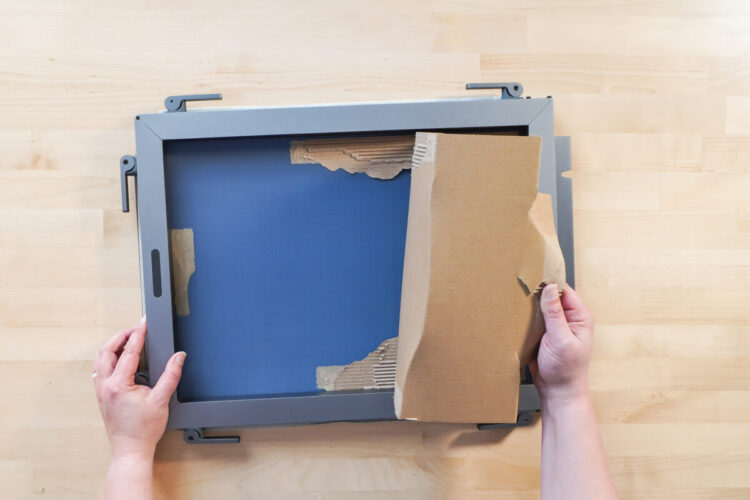 Hands removing the cardboard from the back of a screen printing screen