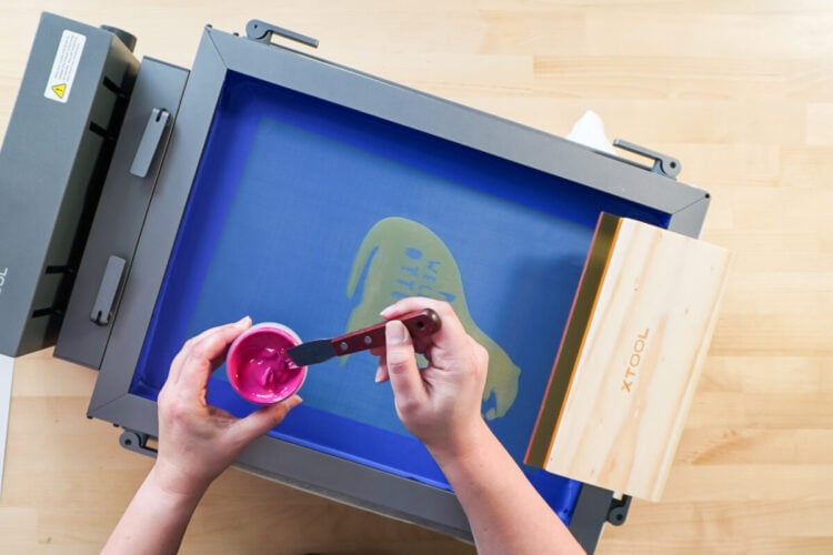 Hands using brush to add paint to the design of an otter on the xTool Laser Screen Printer