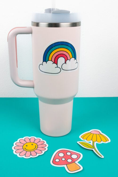 Stanley tumbler with rainbow sticker and other stickers on table