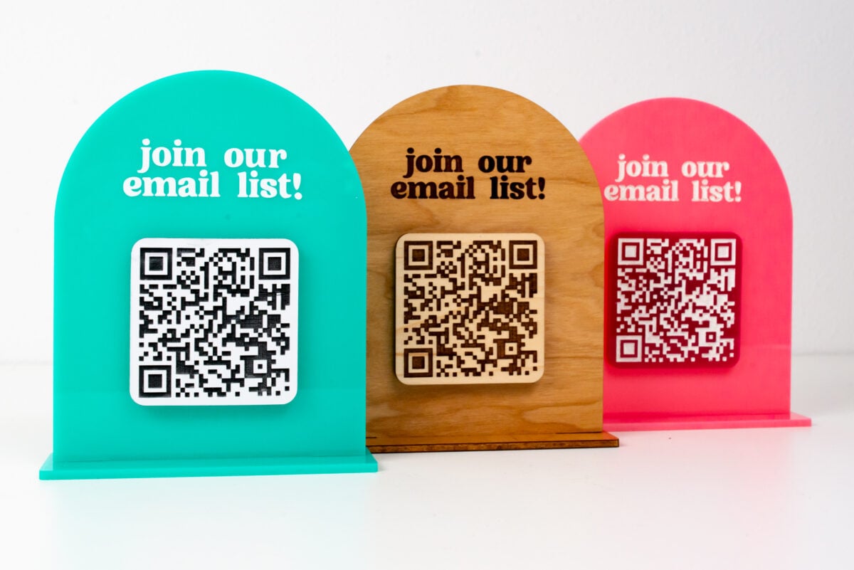 Three QR code signs in teal, wood, and pink
