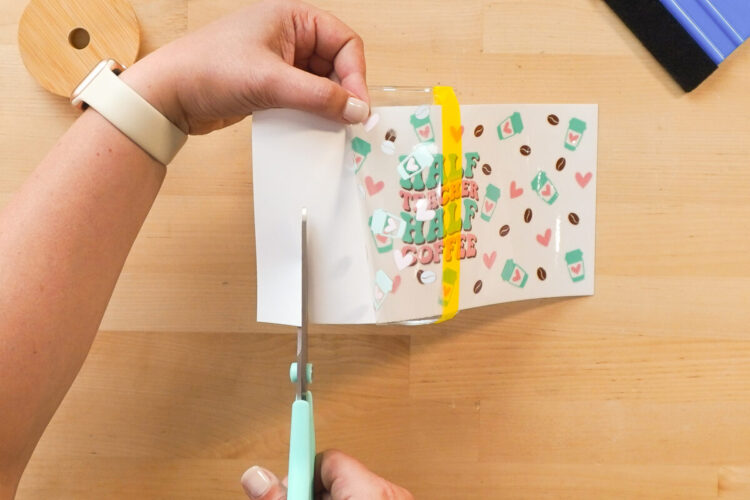 Hands holding a scissors and cutting the backing away from the cup wrap.