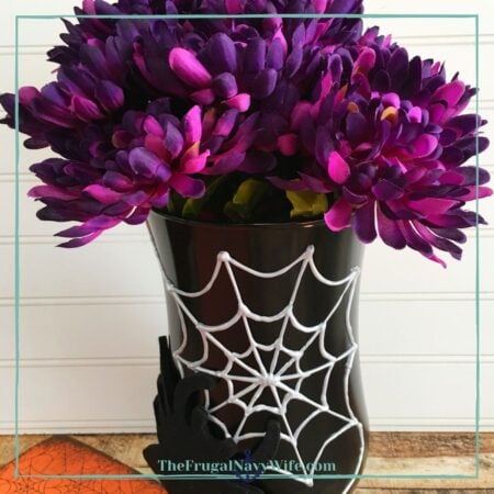 A black vase decorated with a spider web and holding dark purple and pink flowers