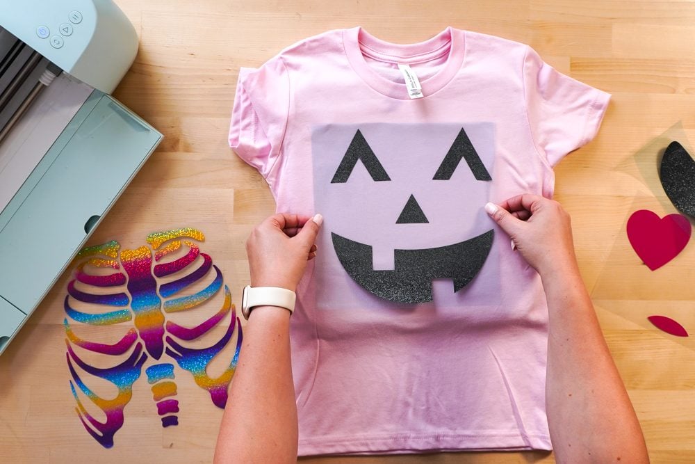 hands placing jack-o-lantern decal on pink shirt