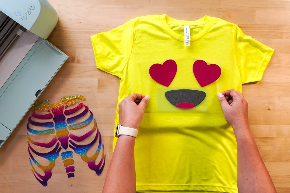 hands placing the two layers of the emoji decal on yellow shirt