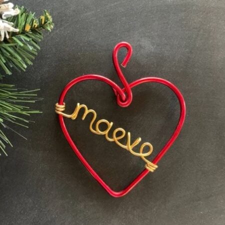 A personalized Christmas ornament in the shape of a heart and with a person's name on it.