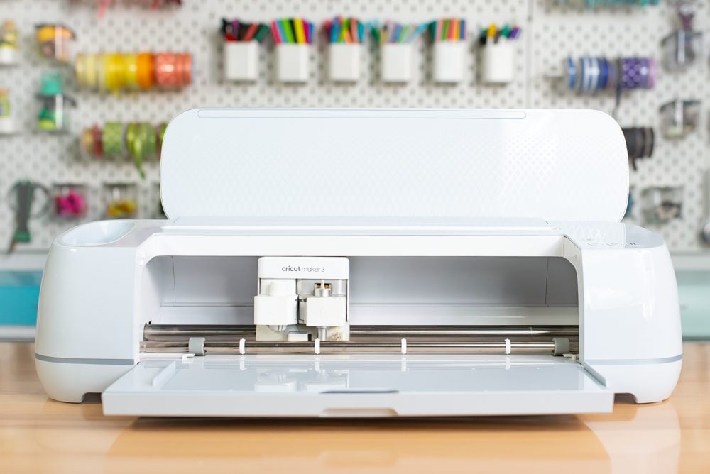 Cricut Maker 3 open on a table with a peg board behind it.