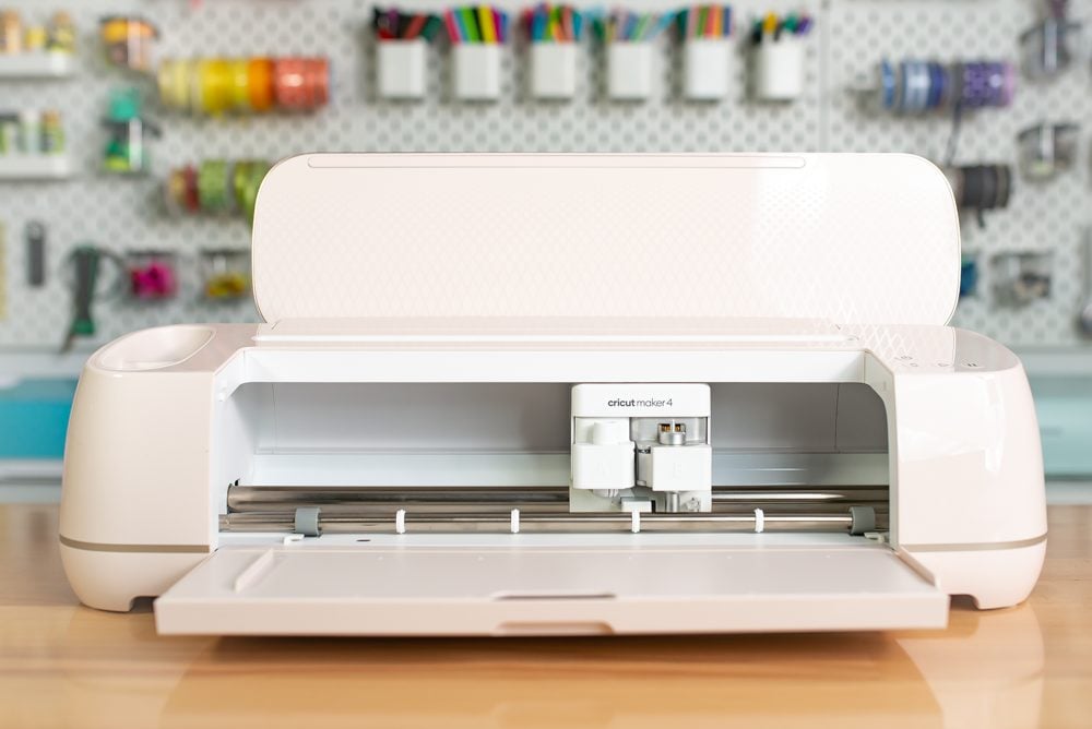 Cricut Maker 4 open on a table with a peg board behind it.