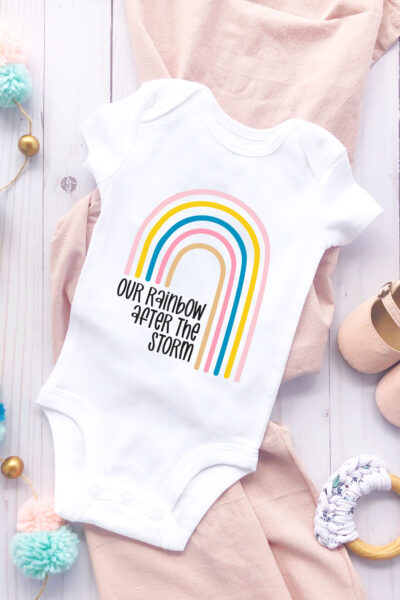 Our Rainbow After the Storm SVG on a onesie with baby accessories
