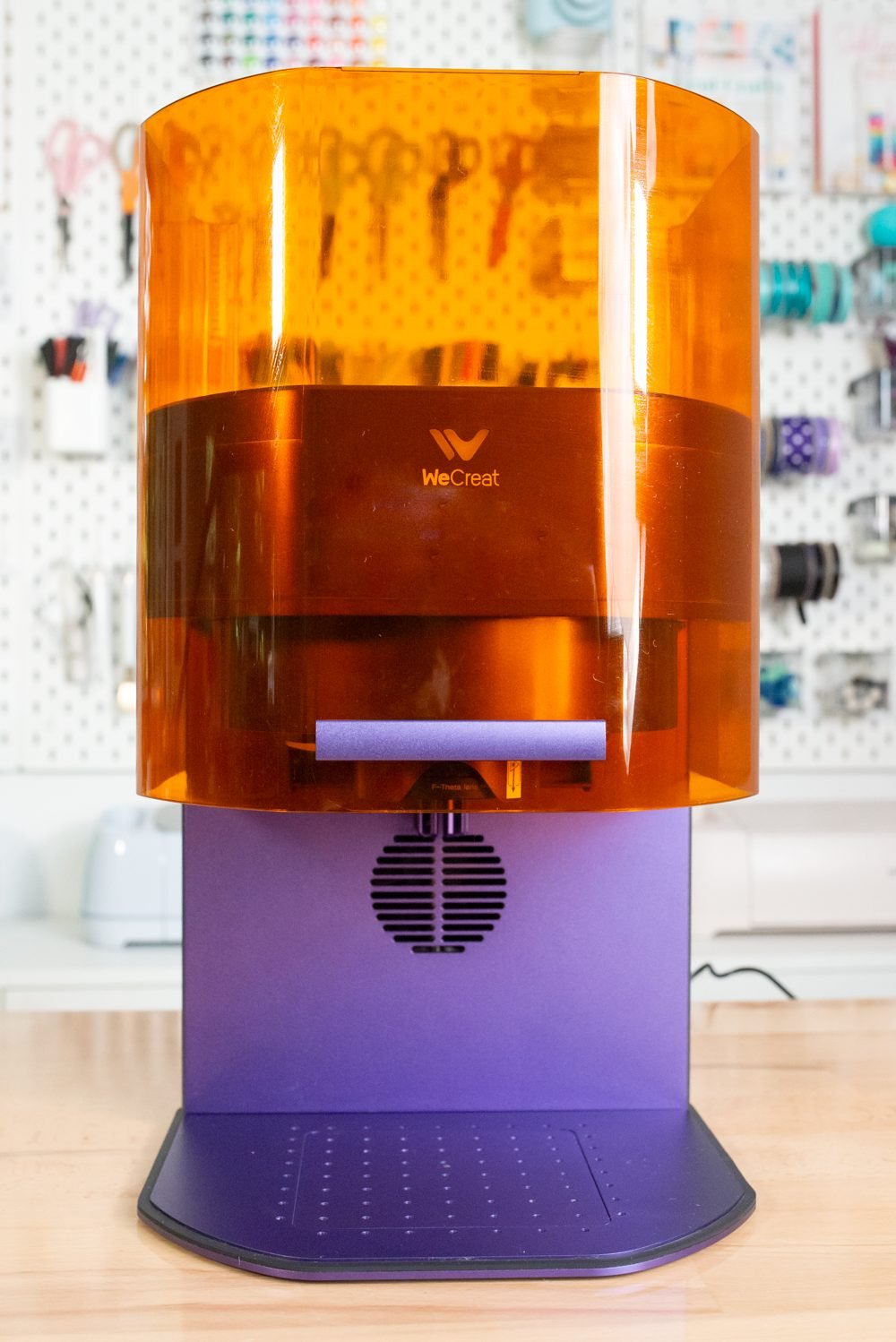 Open WeCreat Lumos machine on a desk in front of a pegboard full of craft supplies