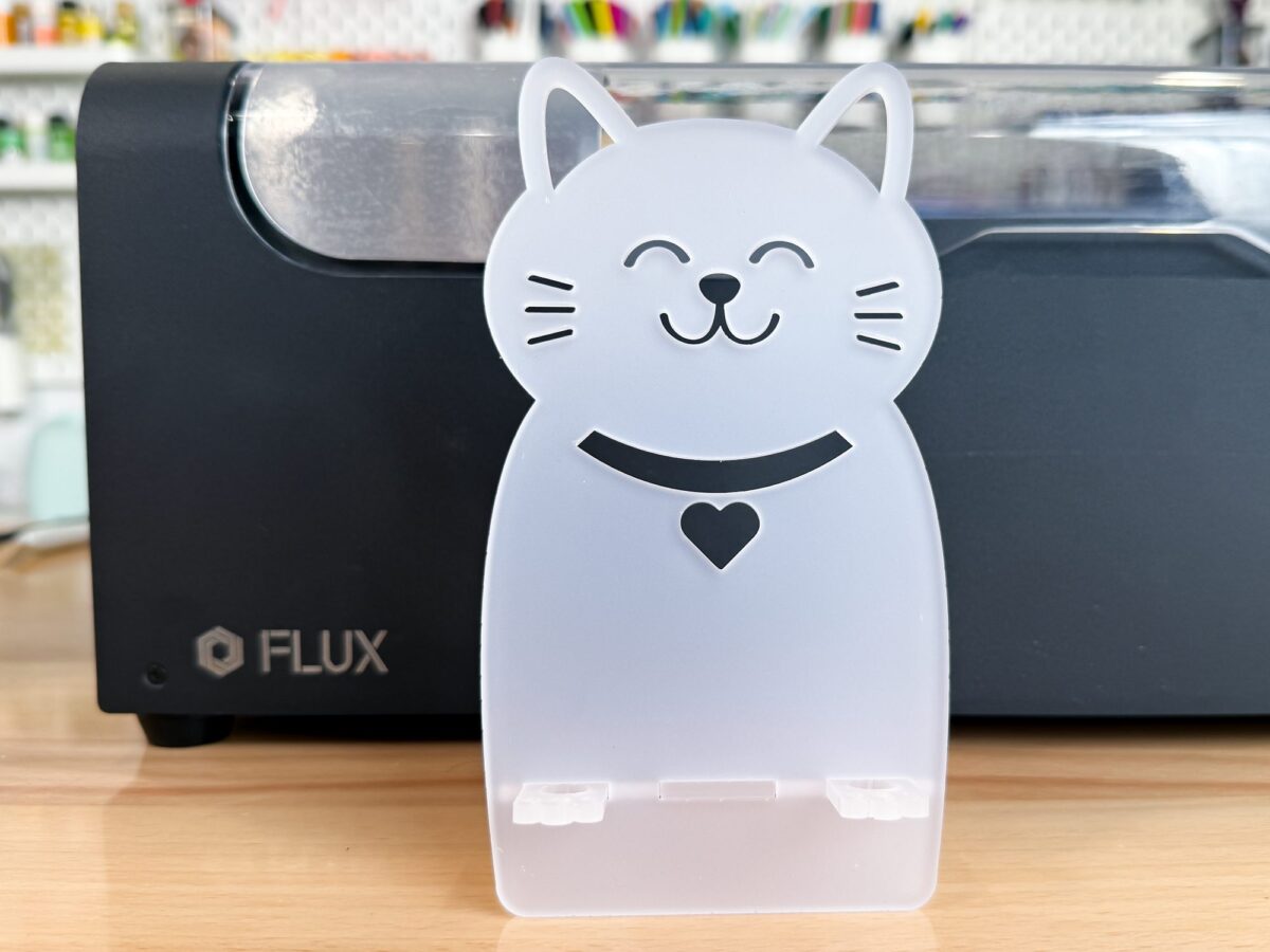Cat phone holder made out of clear acrylic in front of the FLUX beamo