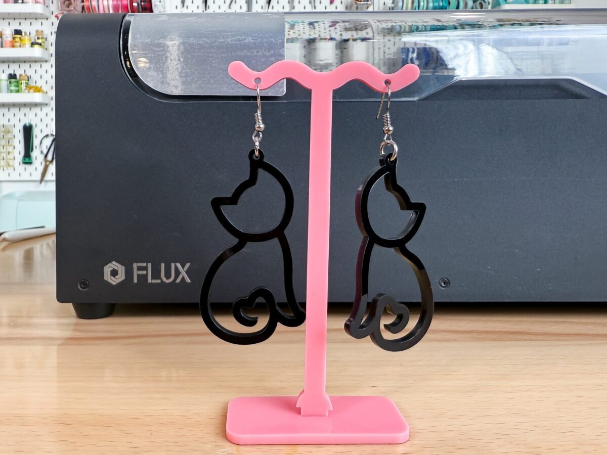 Cat earrings made out of black acrylic in front of the FLUX beamo