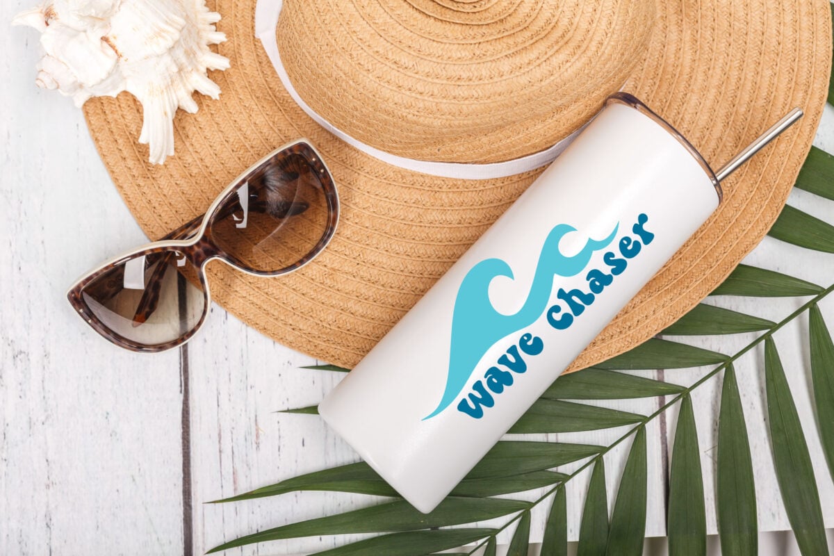Wave Chaser SVG on a white tumbler surrounded by beach gear