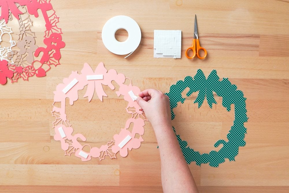 Hands applying foam strips to the back of the pink cardstock layer