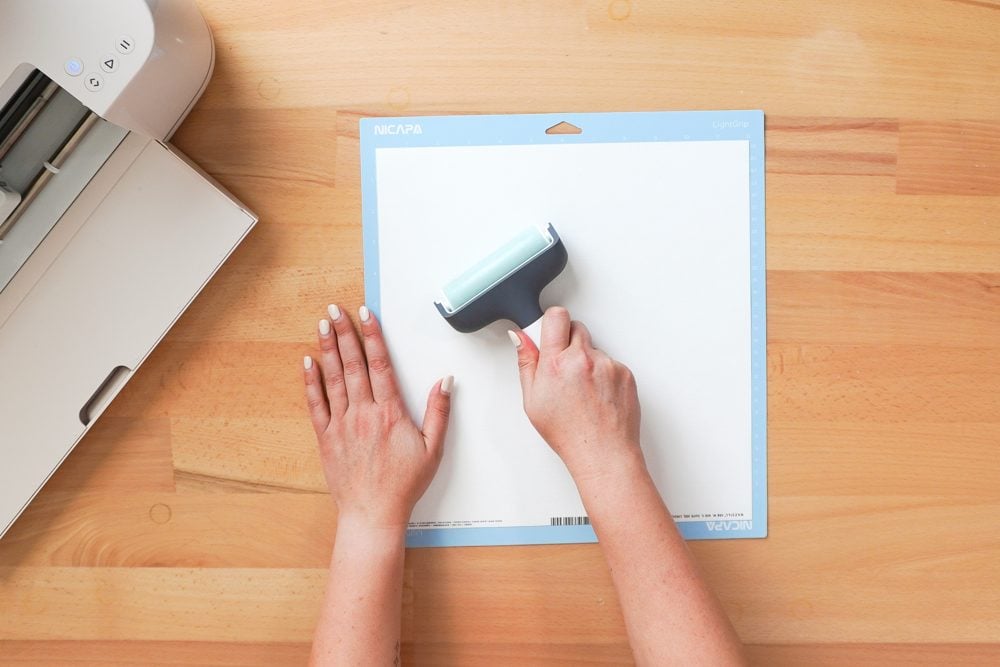 Hands using a brayer to adhere white cardstock to a Cricut mat