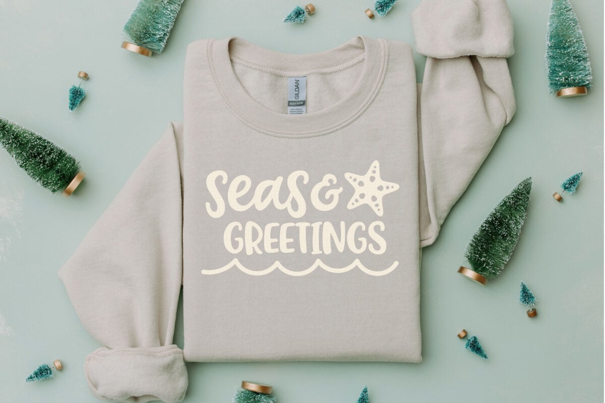 Seas & Greetings Christmas Beach SVG on a gray sweatshirt with Christmas decorations