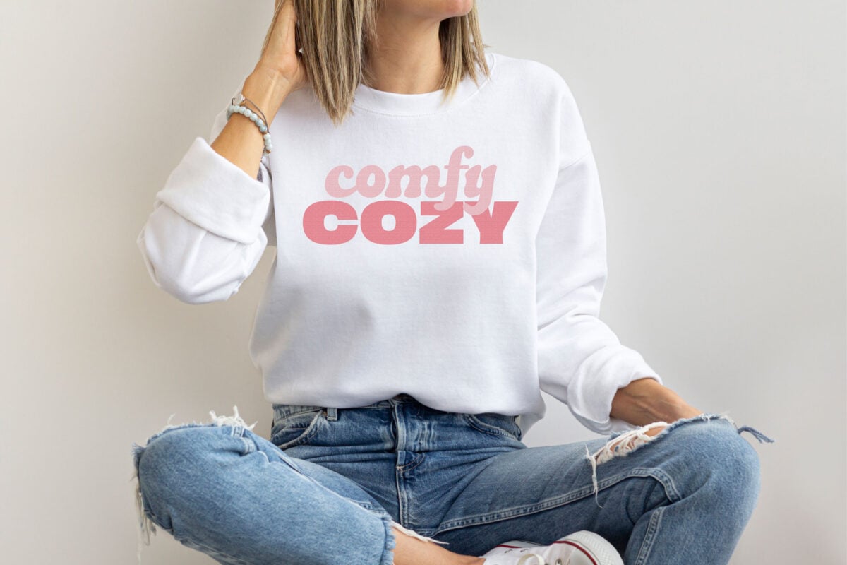 Comfy Cozy SVG on a white hoodie being worn by a white woman with her legs crossed