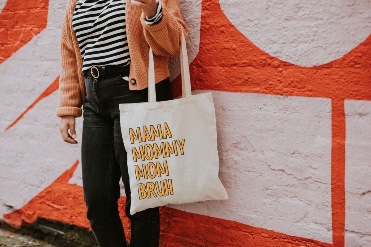 Mama, Mommy, Mom, Bruh SVG on a tote bag in front of a orange wall
